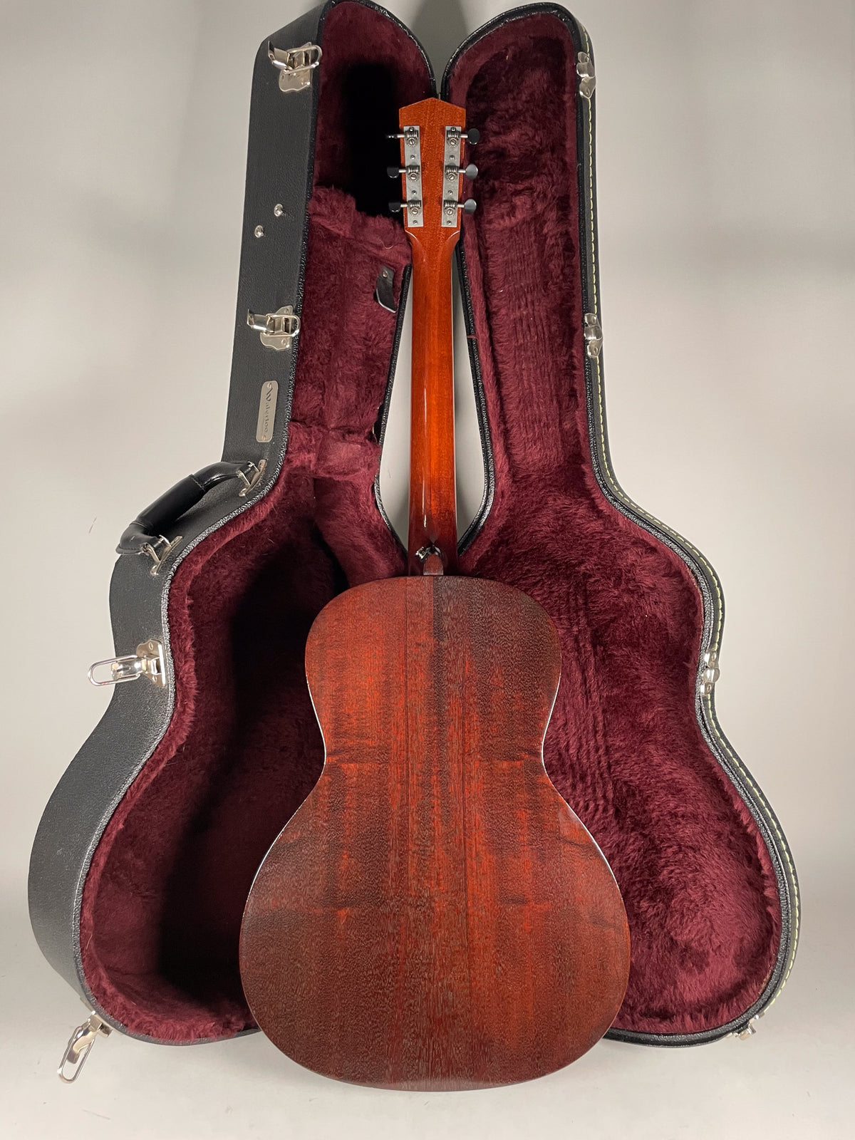 The guitar's dark reddish-brown back and neck are visible, with its headstock and tuners framed by an open hard case.