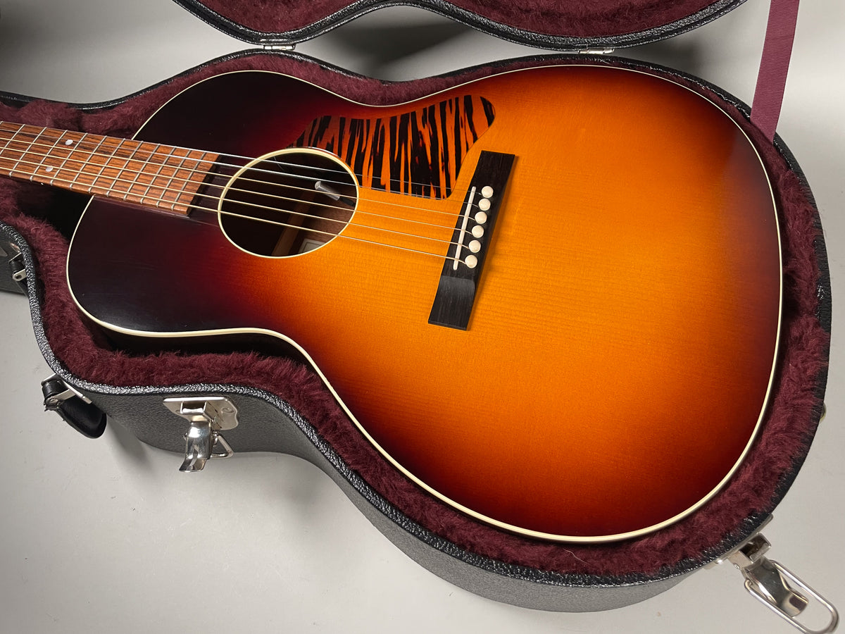 A sunburst acoustic guitar in a hard case, angled to show the body, soundhole, bridge, and striped pickguard.