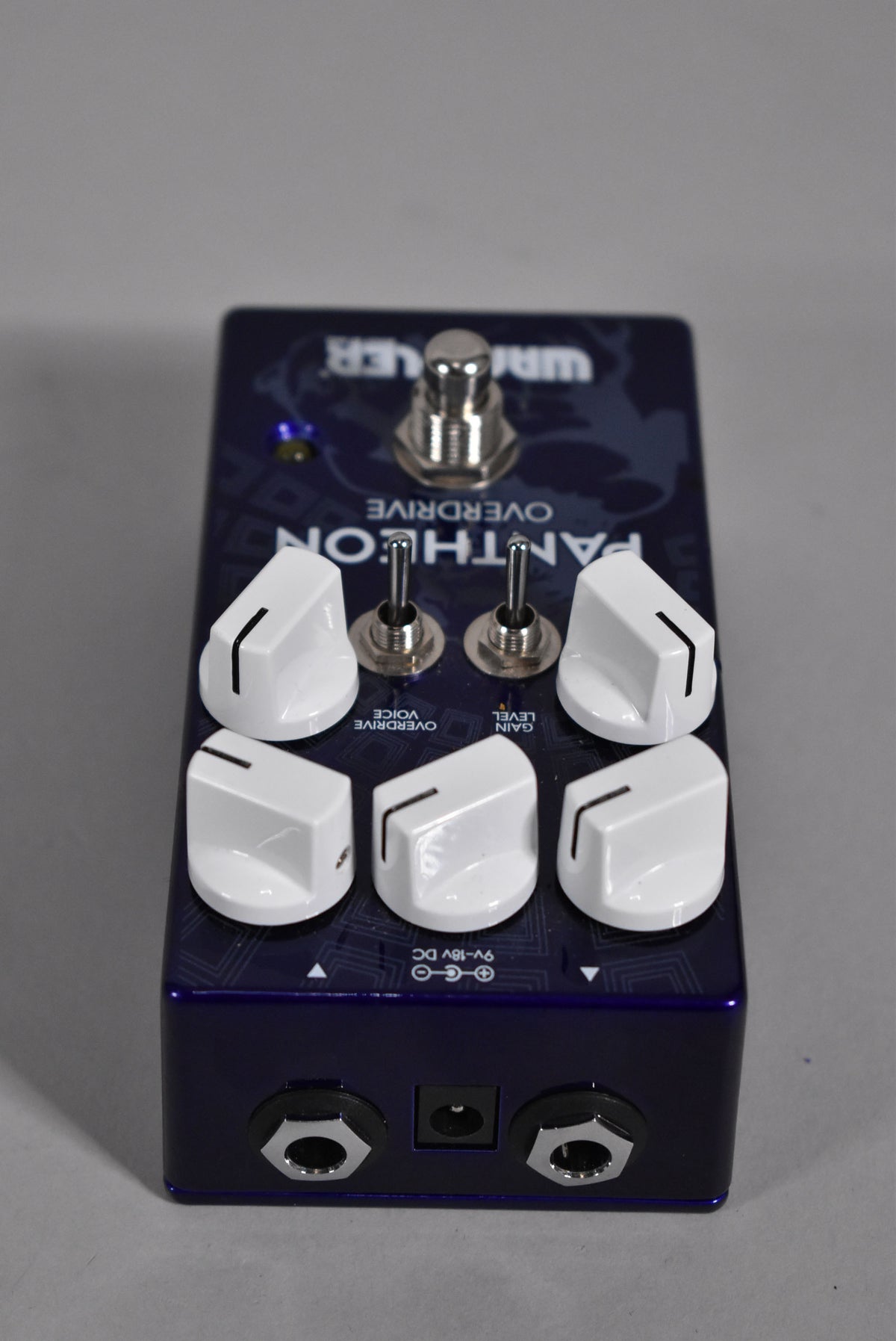 A dark blue pedal with six white knobs, two toggle switches, and a footswitch, viewed from a high angle.