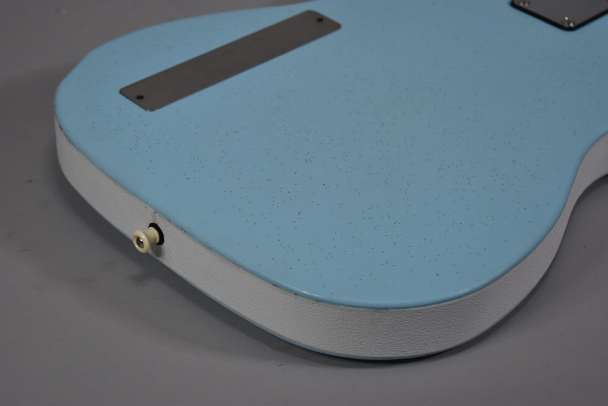 Close-up of the lower body of a light blue guitar with a textured white side, showing the output jack and two metal plates.