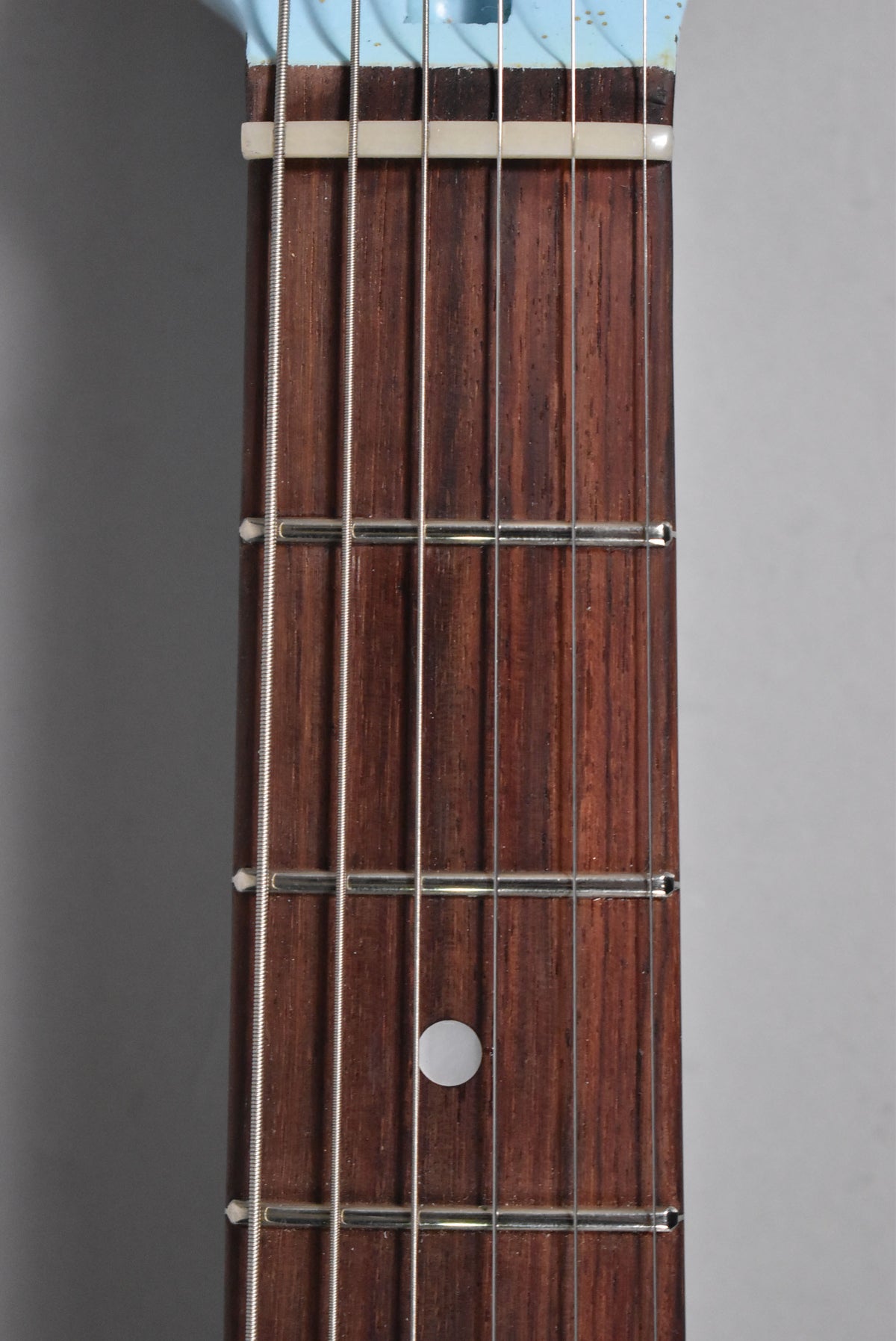 Close-up of the dark rosewood fretboard with six strings, silver frets, and a white dot inlay on the 7th fret.