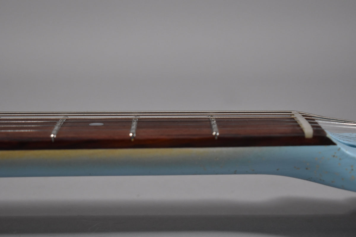 The guitar's neck, with a dark fretboard and light blue finish, shows wear and a cream nut at the headstock end.