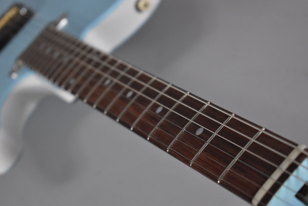 Close-up of the electric guitar's dark fretboard with oval fret markers, angled from the nut to the light blue body.