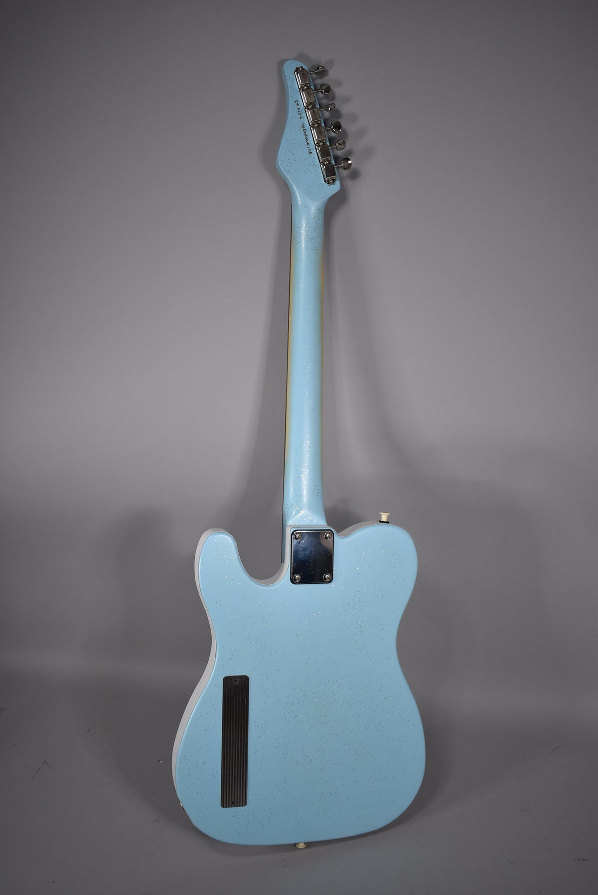 Full rear view of a light blue sparkle guitar with a black neck plate and a long black tremolo cover.