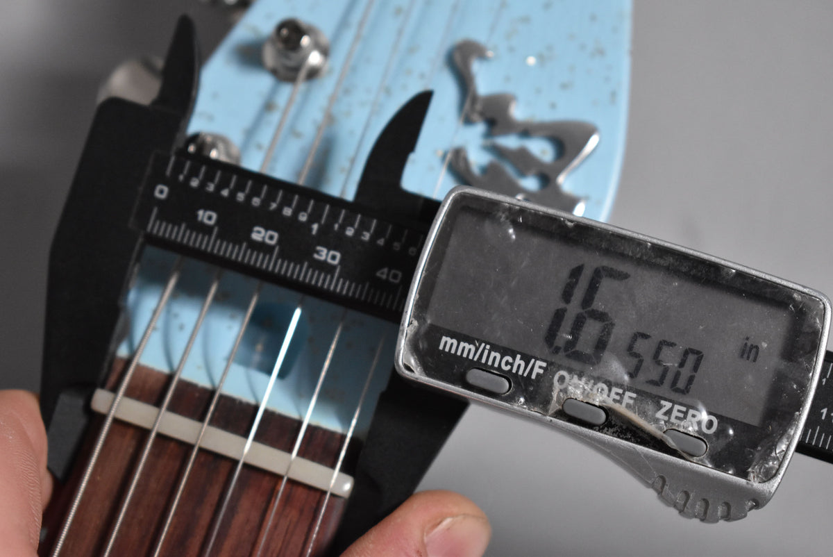 A digital caliper measures the nut width of the Sonic Blue guitar's dark fretboard at 1.655 inches.
