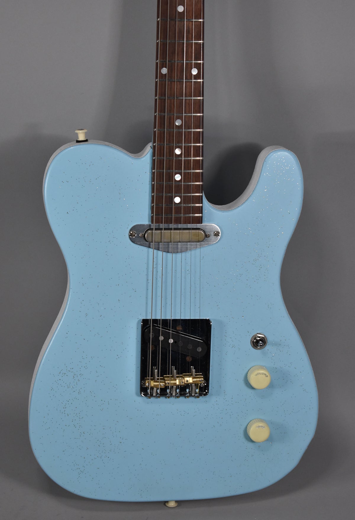 Full-frame view of a light blue sparkle electric guitar with a dark fretboard, gold bridge, and cream control knobs.