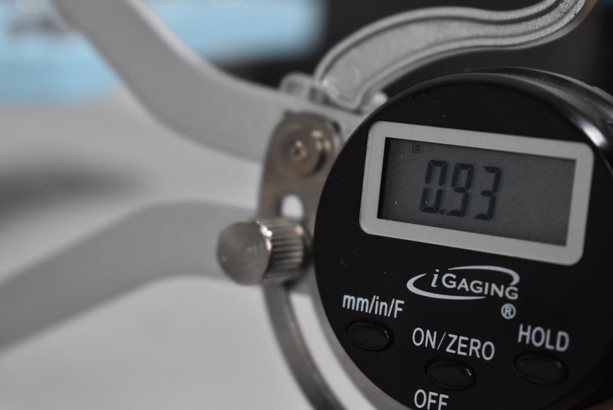 Close-up of a digital caliper measuring 0.93 inches, with the black display and silver body of the tool in focus.