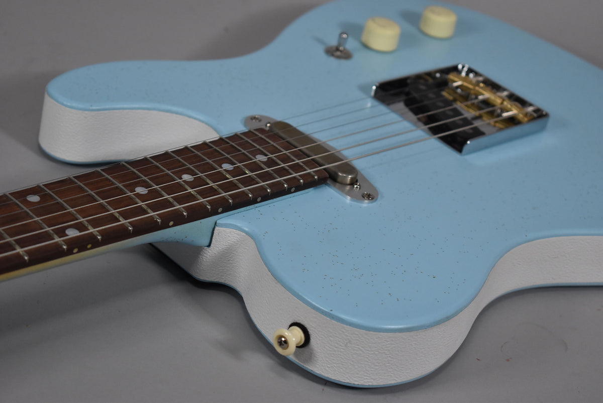 The light blue electric guitar body, with white textured sides, shows a dark fretboard, chrome bridge, and cream knobs.