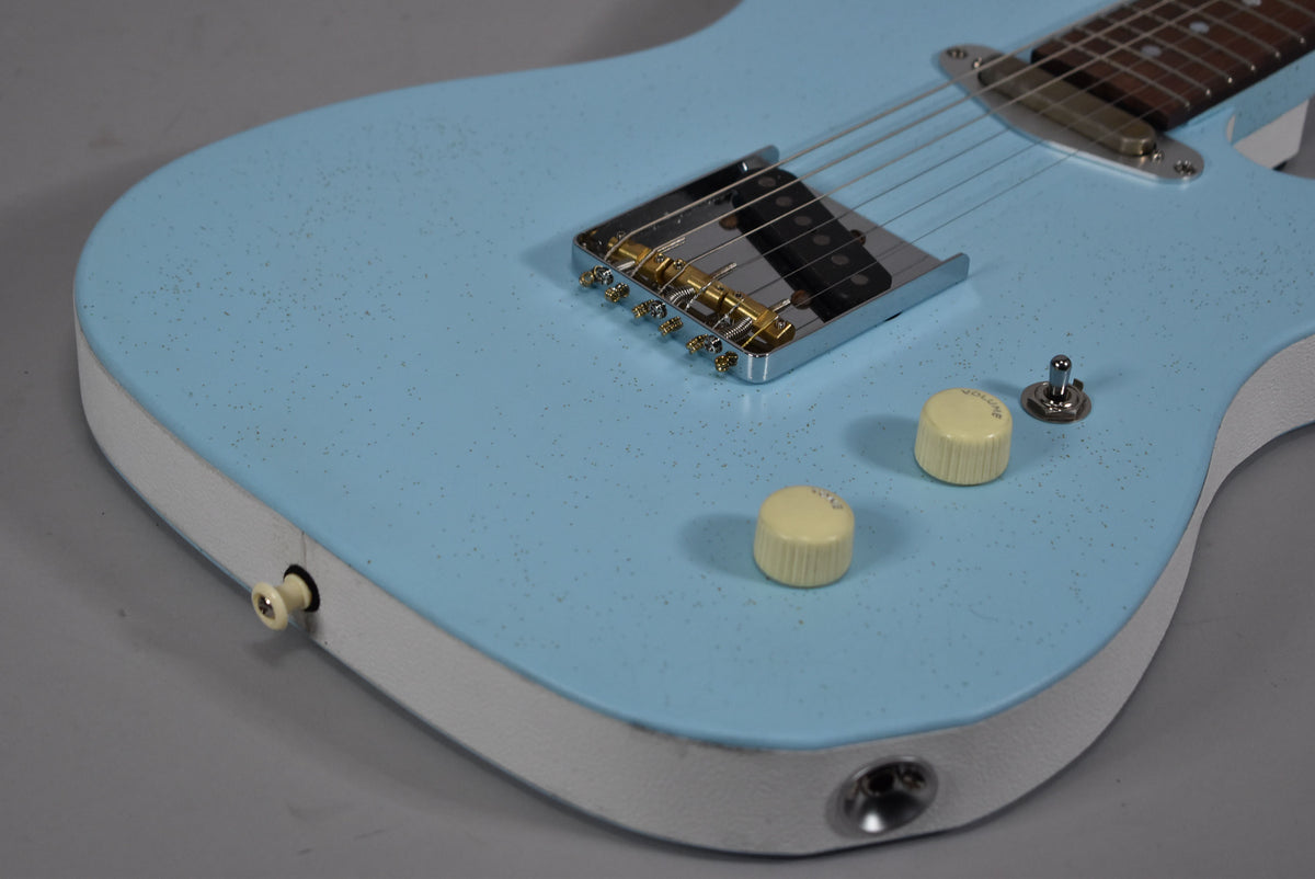 Close-up of the light blue sparkle body with white binding, showing the bridge, two cream knobs, a toggle switch, and input jack.