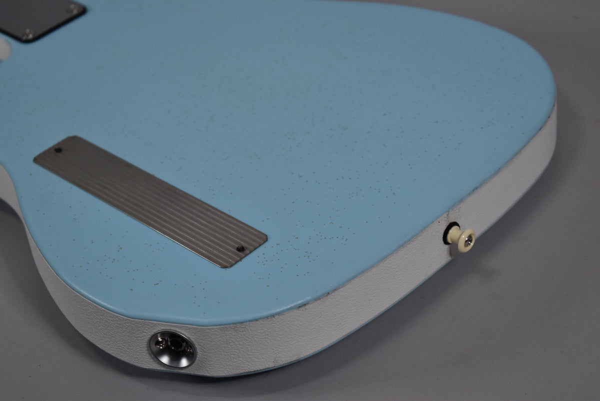 The back of a light blue guitar with a white textured edge, showing a long metal plate and two strap buttons.