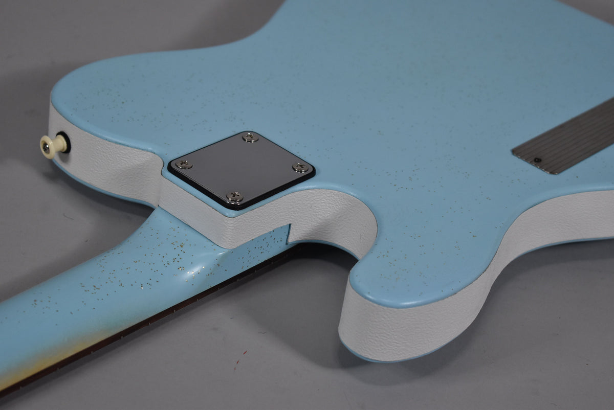 The back of a light blue guitar with white binding, showing the neck joint, output jack, and a metal neck plate.