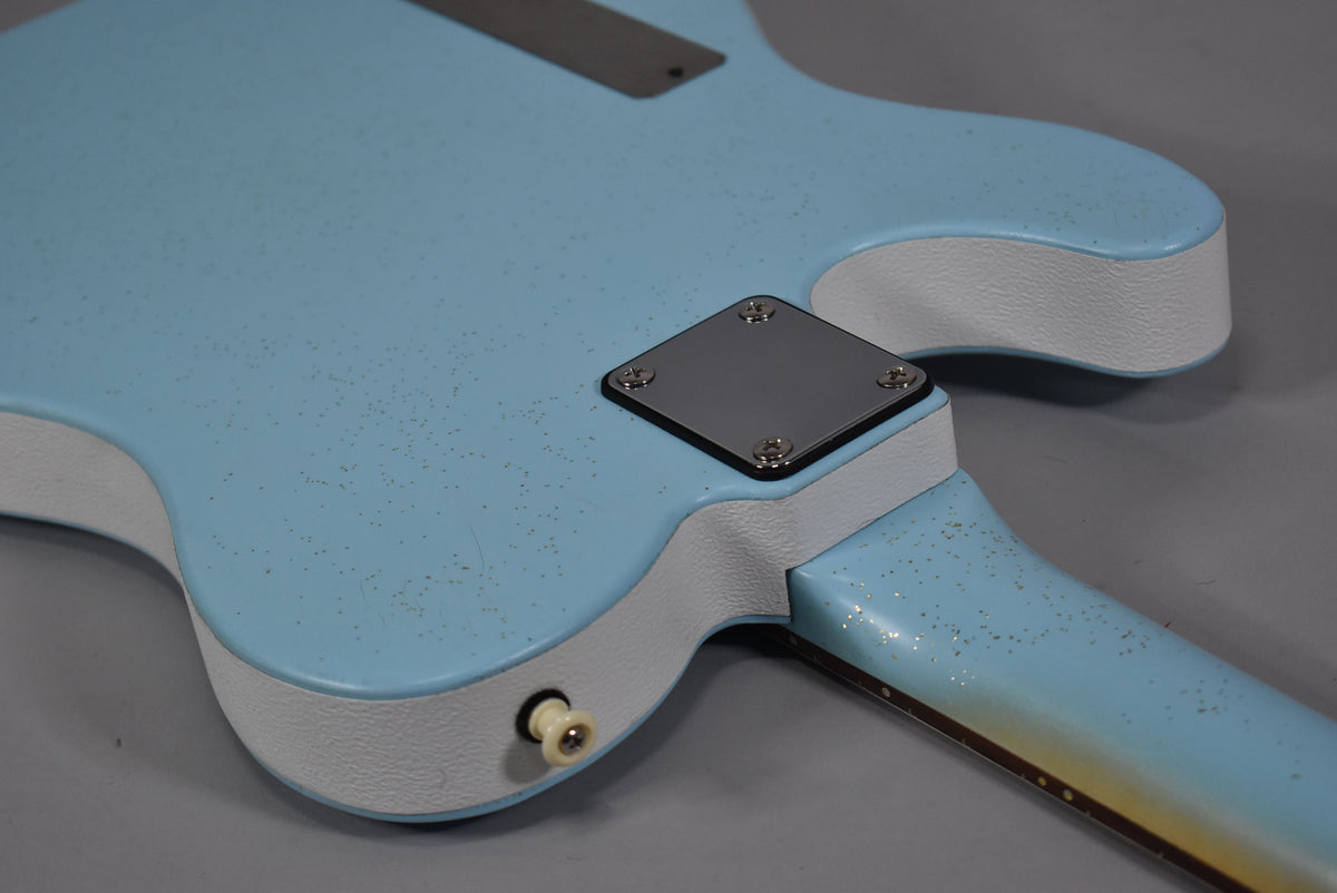 The back of a light blue guitar body with white sides, showing a chrome neck plate and a cream output jack.