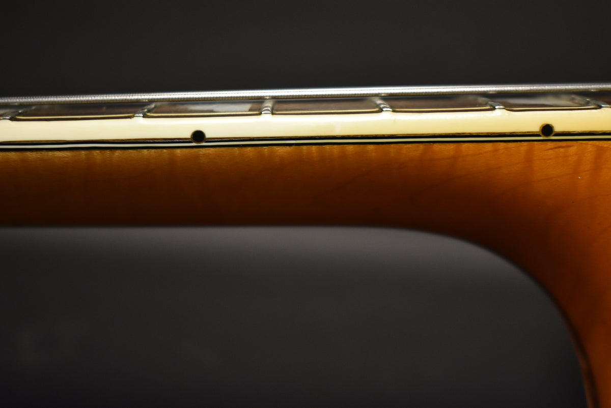 Close-up of the guitar's neck, showing the light-colored binding with black side dots and a natural wood finish on the neck.