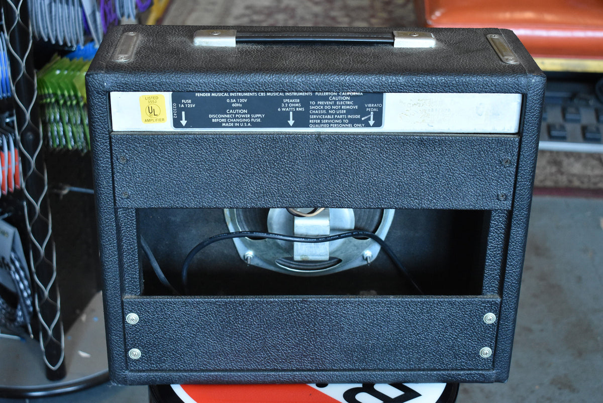 Rear view of a black textured combo amp, showing the exposed speaker, metal chassis, and top handle.