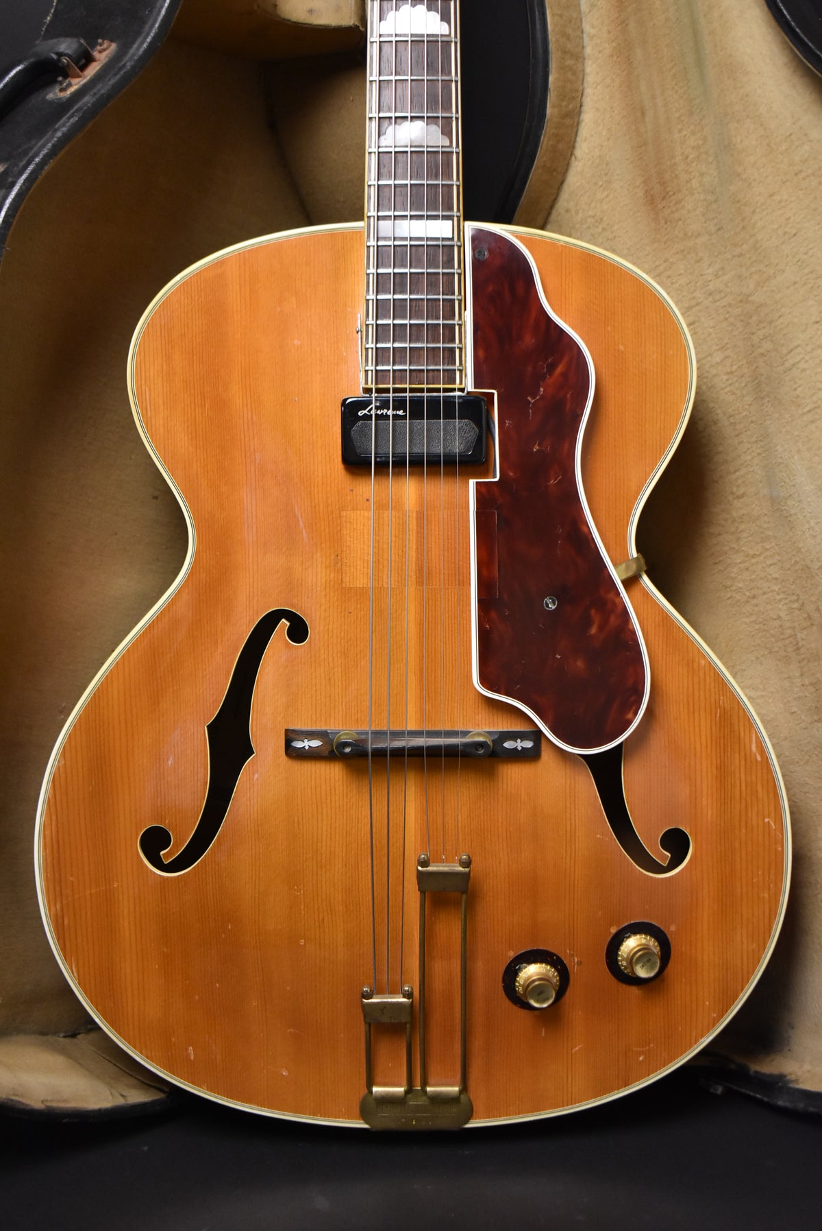 Full-frame view of a natural finish archtop guitar, showing a dark tortoise pickguard, floating pickup, and two gold knobs.