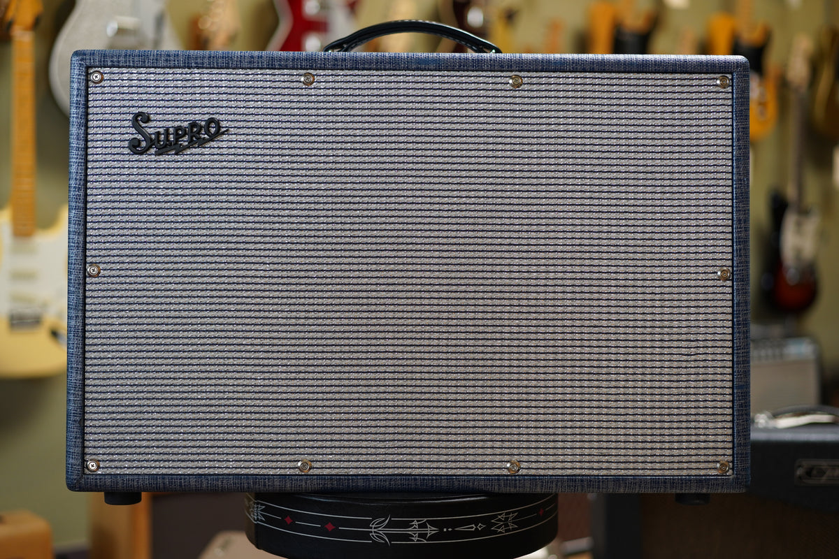 Front view of a blue-gray tweed amp with a silver and black striped grille cloth, black handle, and eight silver screws around the grille.