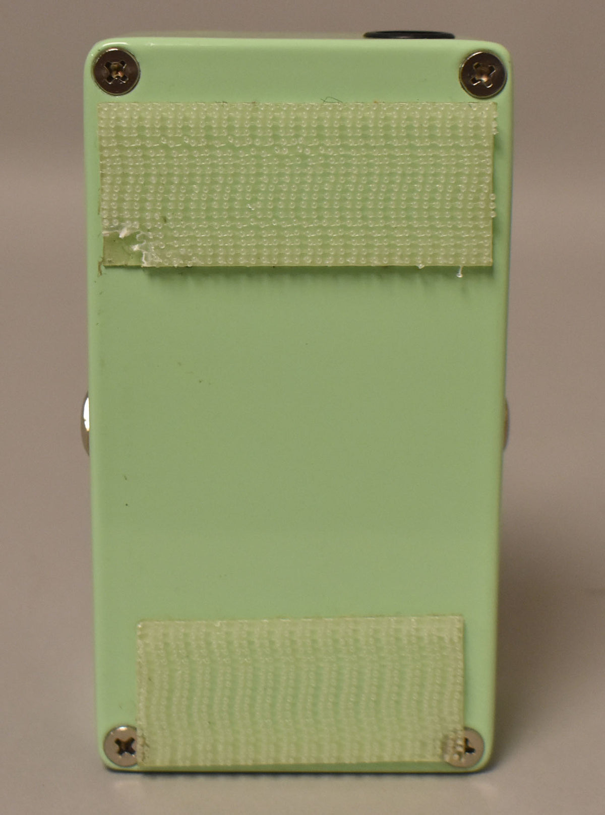 The green effect pedal's bottom is shown, with two strips of light green hook-and-loop fastener and four silver screws.