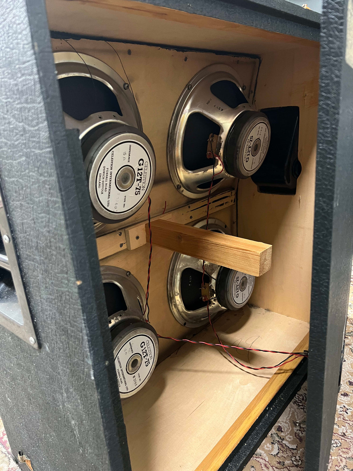 An angled view inside the black cabinet, revealing four silver-coned speakers with visible wiring and a wooden brace.