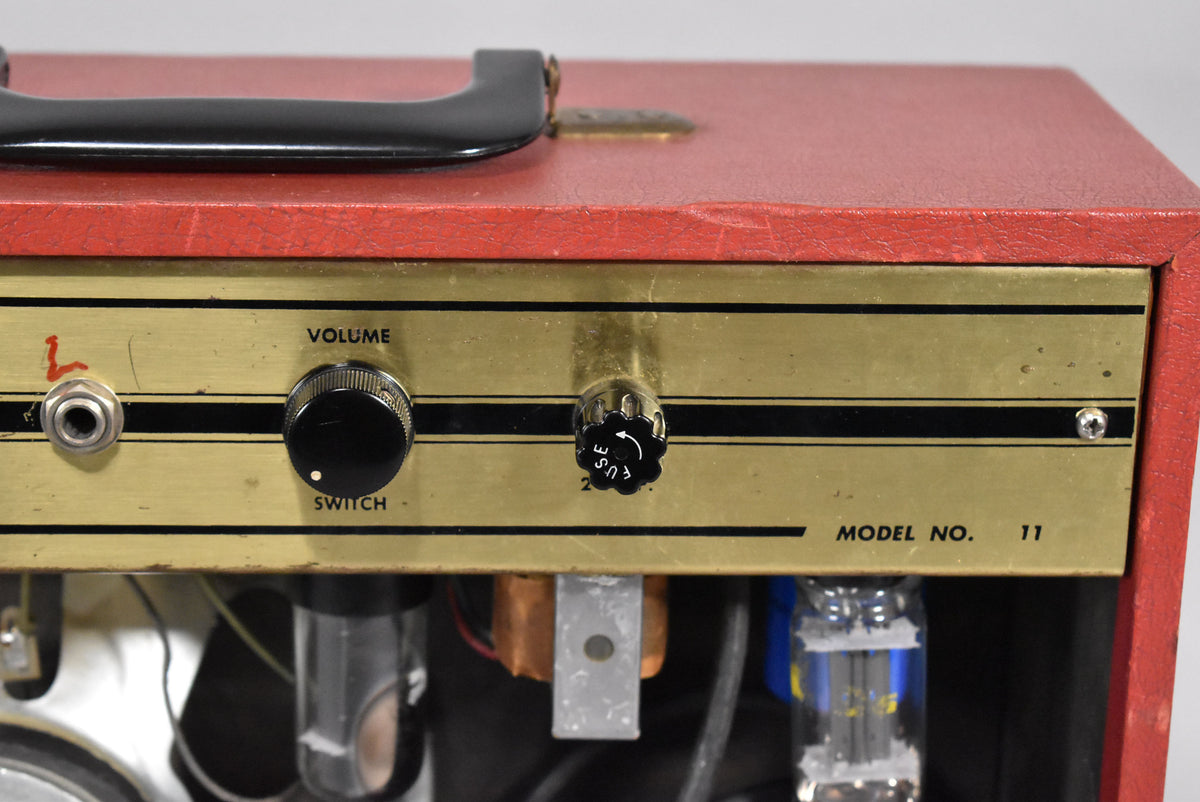 Close-up of the red amp's gold control panel, showing a black Volume knob, a fuse cap, and an input jack with red paint around it.
