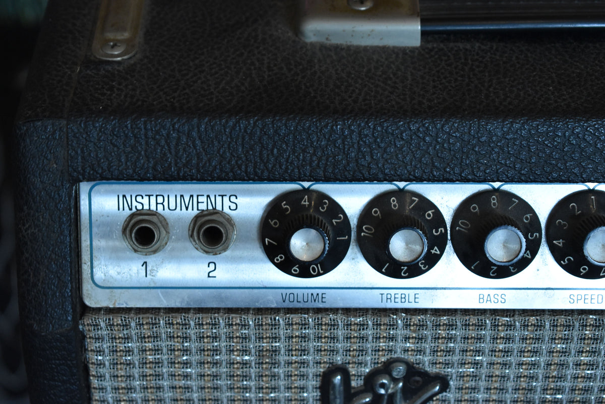 Close-up of the black tolex amp's silver control panel with two inputs, four black knobs, and a woven speaker grille below.