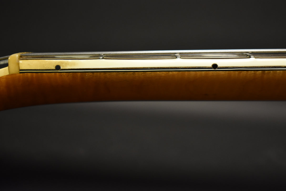 Close-up of the guitar's neck, showing the light brown wood, cream binding, and two black dot fret markers.
