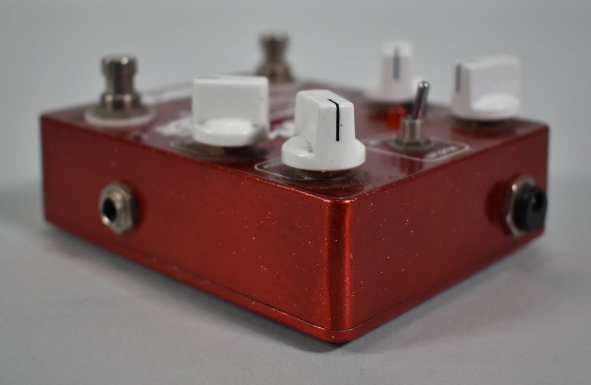 A red glitter-finish pedal, viewed from the front right, showing white knobs with some scuffs, a toggle switch, and input jacks.