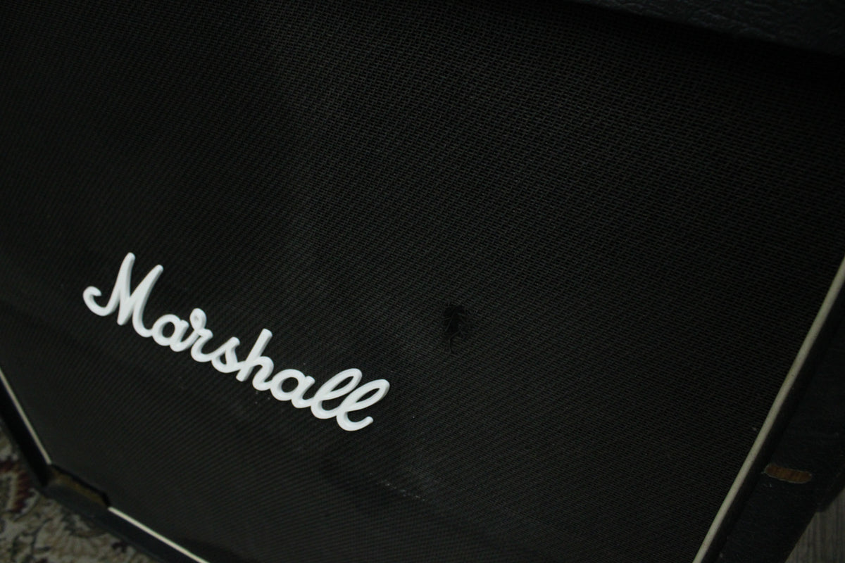 Close-up of the black speaker grille cloth with a small tear, showing the white script logo and white piping along the cabinet's edge.