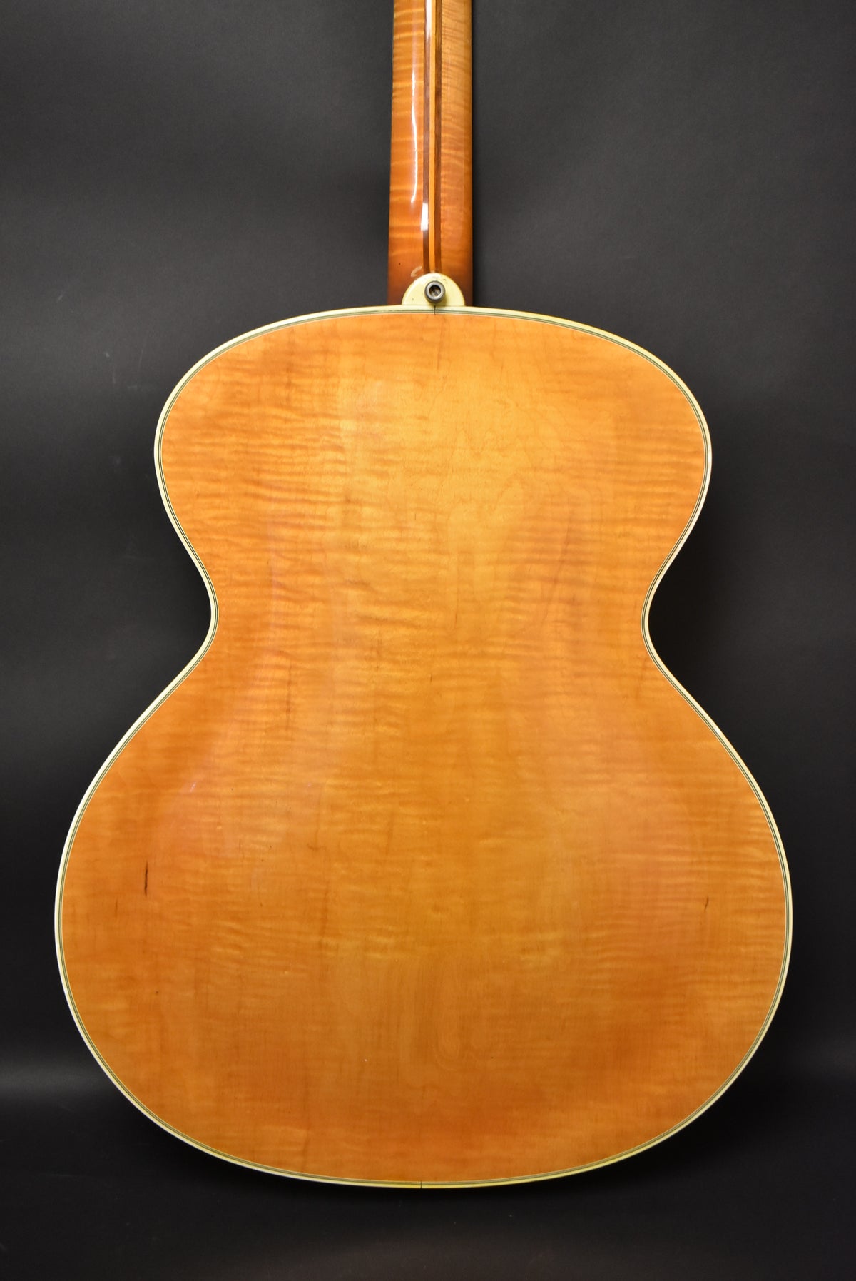 The guitar's back is a light amber, flamed maple with a glossy finish, showing some light checking and a single strap button at the neck joint.