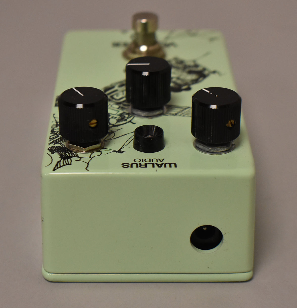 The green effect pedal is angled, showing its right side with a power input and three black control knobs with white indicator lines.
