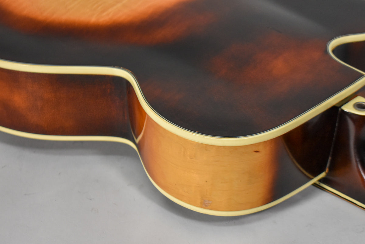 Close-up of the lower bout and waist of the sunburst archtop, showing the cream binding and some wear on the light-colored side.