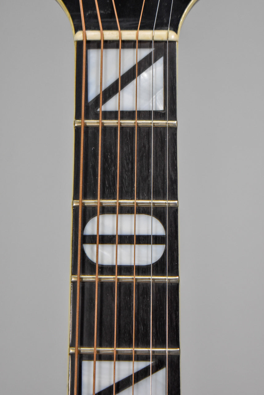 Close-up of the dark fretboard with mother-of-pearl inlays: a horizontal oval and two diagonal triangles, with six strings.