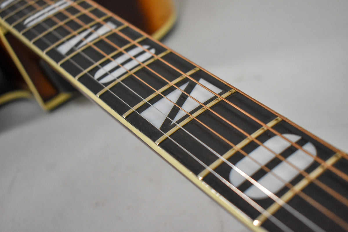 Close-up of the guitar's dark fretboard with large, white, geometric block inlays and copper-colored strings, showing light wear.