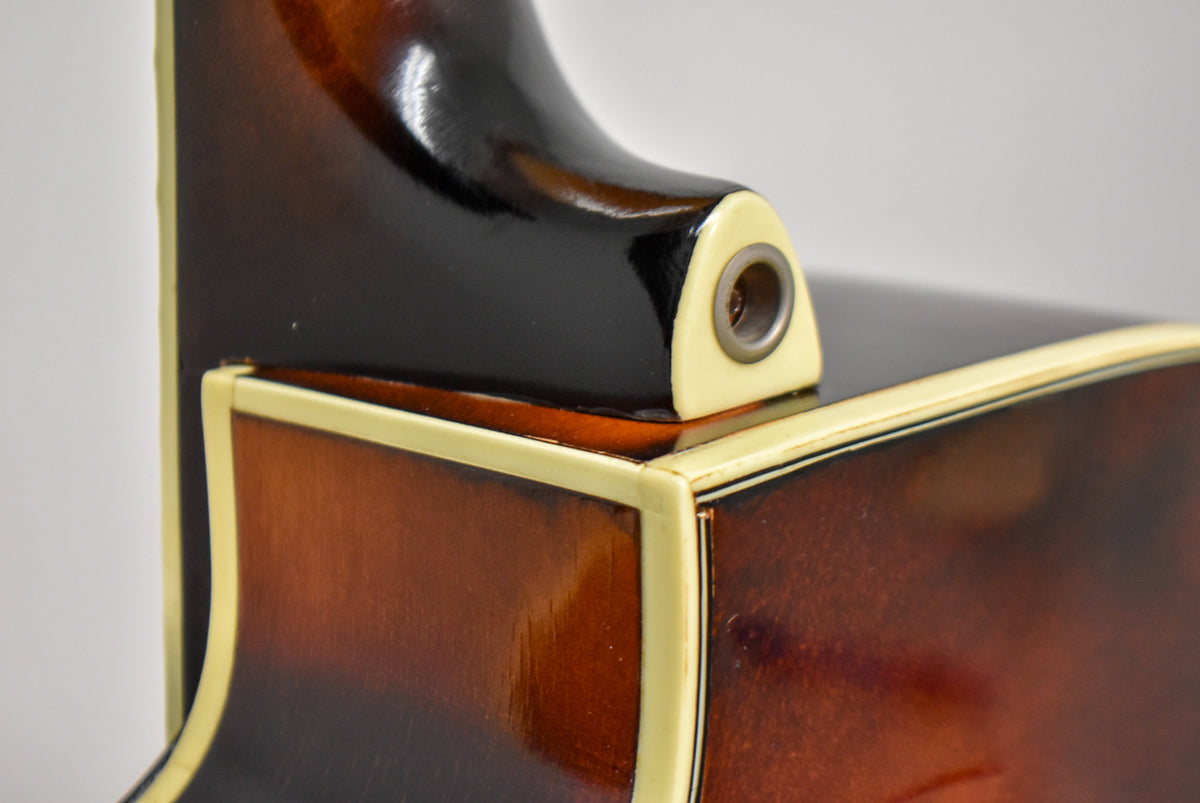 Close-up of the guitar's sunburst body and black neck heel, showing cream binding, a strap button, and light finish wear.