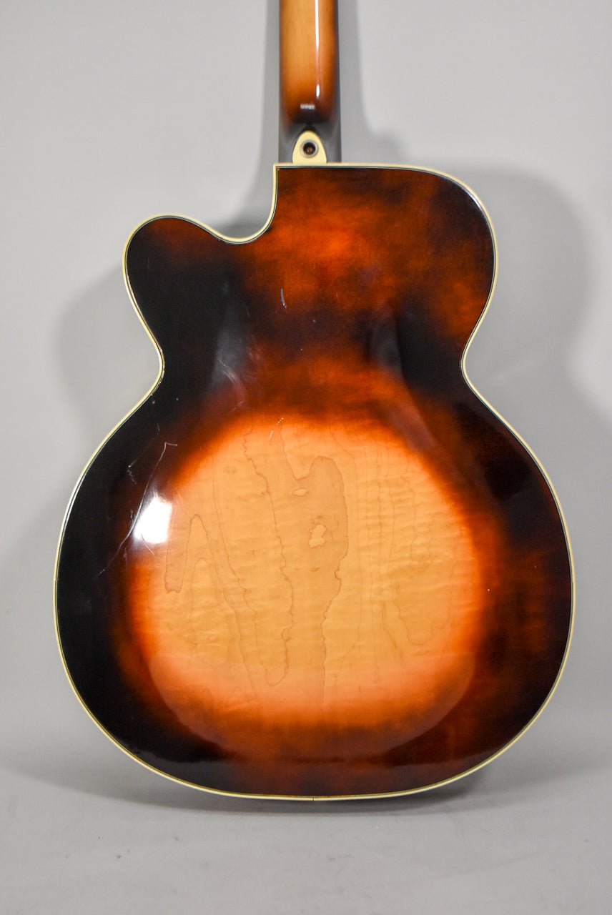 The guitar's sunburst back shows a light maple center fading to dark brown, with visible finish checking and wear, and a strap button at the neck heel.