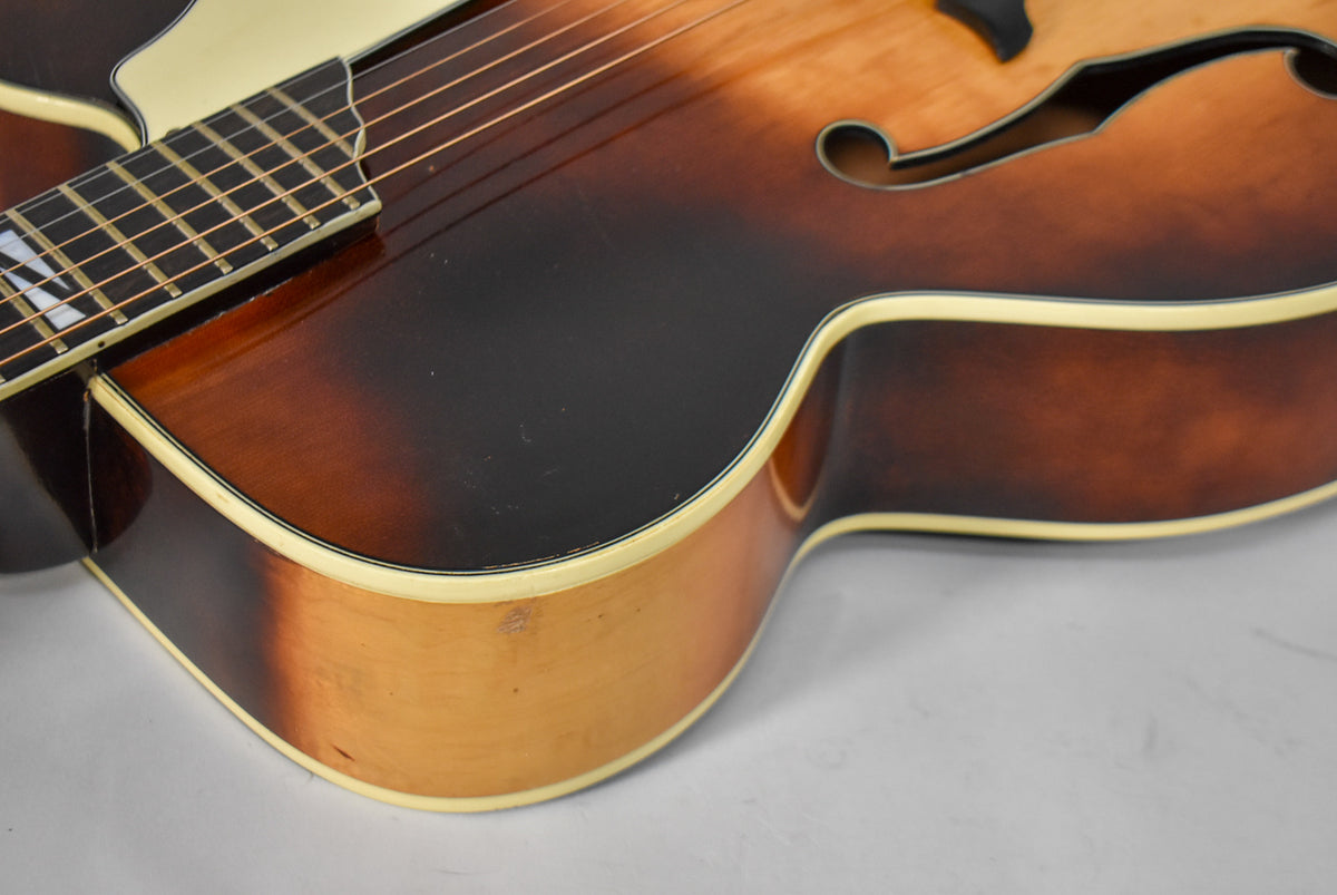 The lower bout of a sunburst archtop guitar, showing the dark brown top, lighter brown sides, and cream binding with wear.