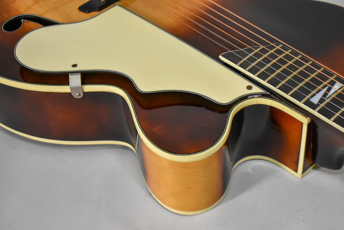 Close-up of the guitar's lower bout and cutaway, showing the sunburst finish, cream binding, and pickguard with a metal bracket.