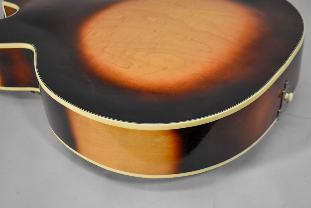The guitar's lower bout and side, showing the sunburst finish with light checking and a cream binding, from a low angle.