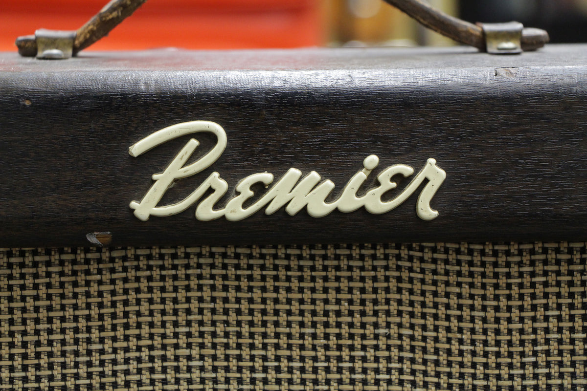 Close-up of the amp's upper front, showing the dark brown wood-grain finish, cream script logo, and woven black and tan grille cloth.