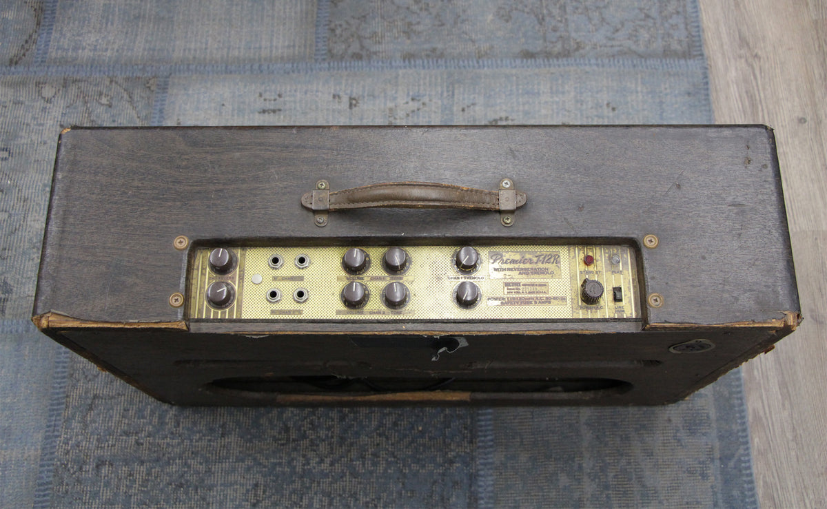 Top-down view of a dark grey combo amp with a worn leather handle and a gold control panel with eight black knobs.