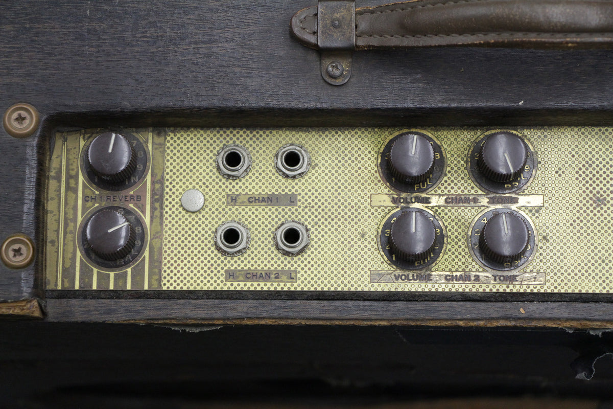 Close-up of the amp's gold control panel with 6 dark grey knobs, 4 input jacks, and a silver button, showing wear and tear.
