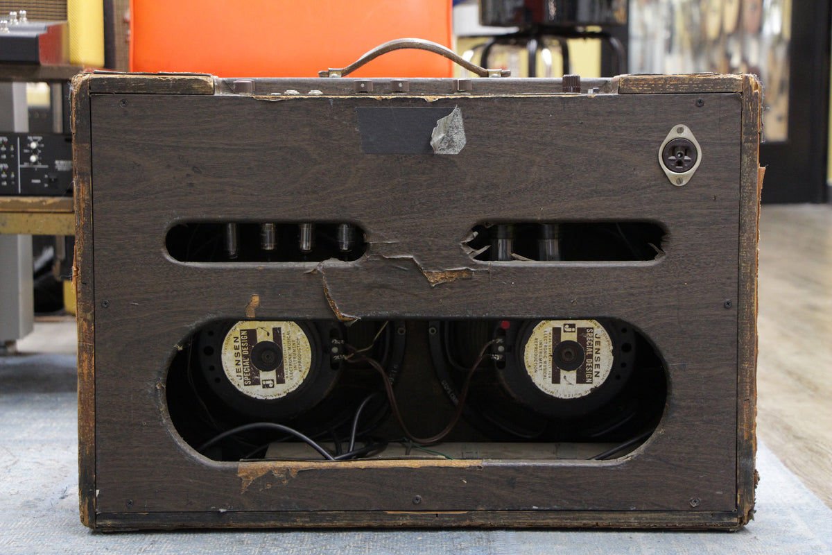 The amp's dark brown wooden back panel is heavily worn and torn, revealing two Jensen speakers and several vacuum tubes.