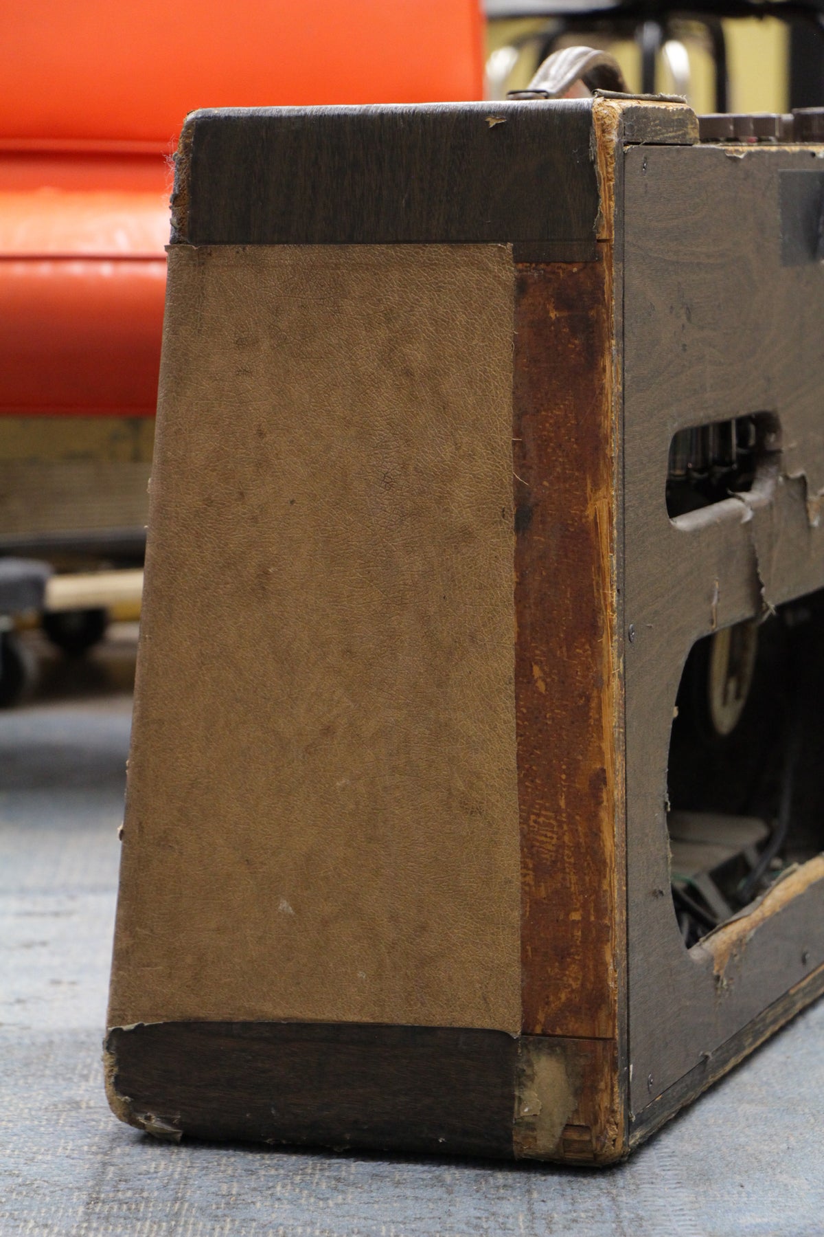 Close-up of the amp's left side, showing the worn dark brown tolex and tan grille cloth, with exposed wood and tears.