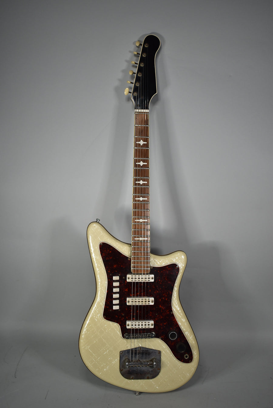 Full-length view of a cream pearl-finish electric guitar with a dark tortoiseshell pickguard, three pickups, and a vibrato tailpiece.