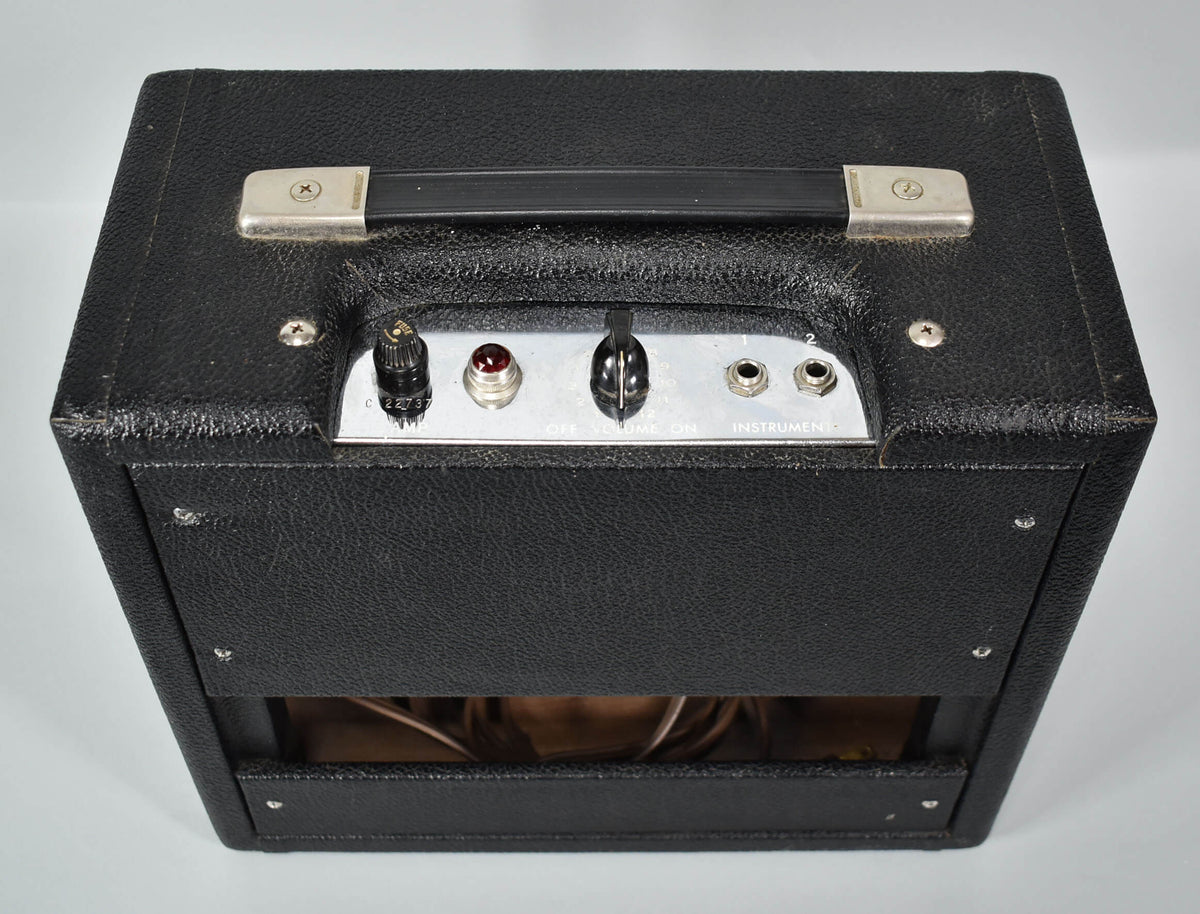 Top-down view of a black combo amp with a silver control panel, black handle, red jewel light, and two input jacks.