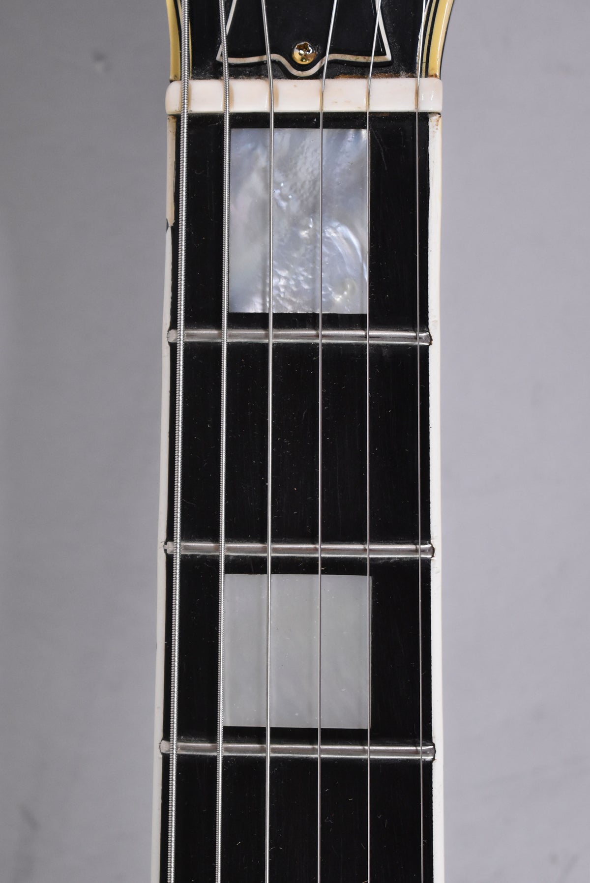 Close-up of the black fretboard with mother-of-pearl block inlays, showing light wear and a cream binding with some checking.
