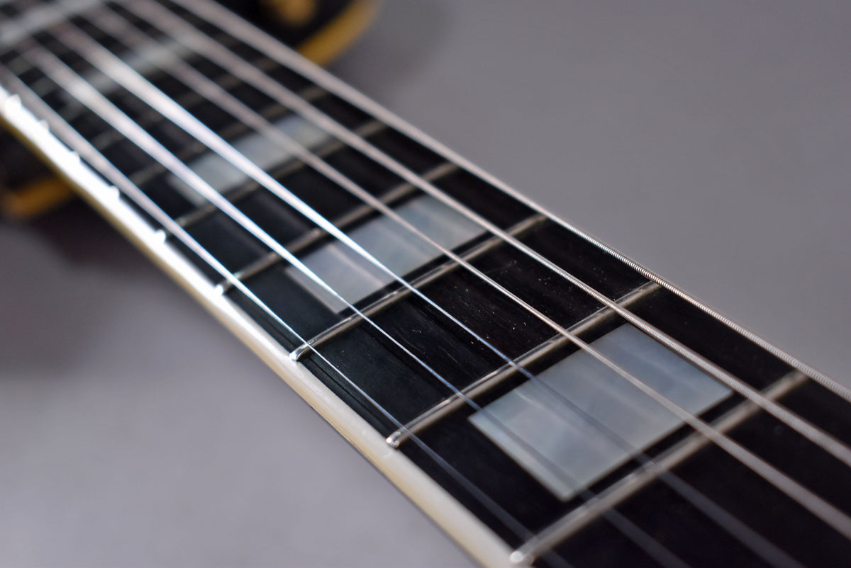 Close-up of the guitar's black fretboard with rectangular pearloid inlays, showing light wear on the frets and strings.