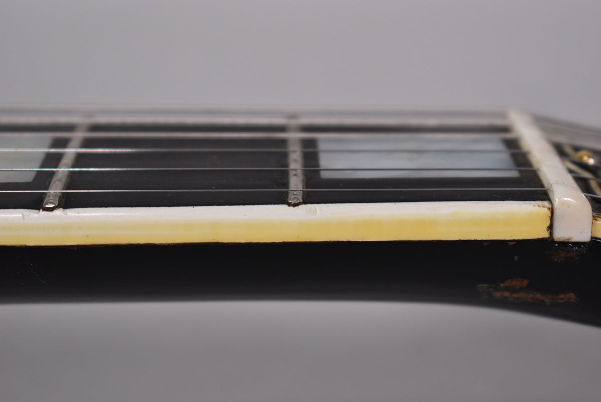 Close-up of the guitar's black fretboard and white binding, showing fret markers, strings, and wear on the binding and neck.