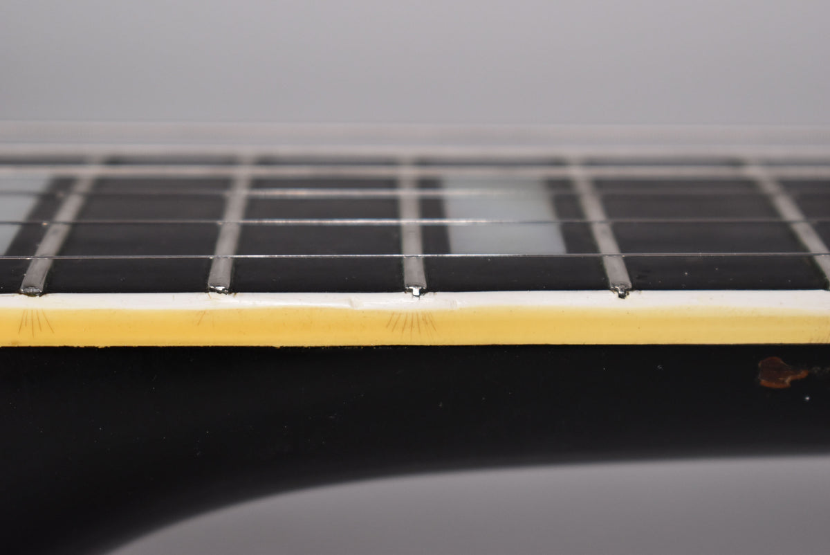 Close-up of the black fretboard and cream binding, showing fret wear and finish checking on the binding.