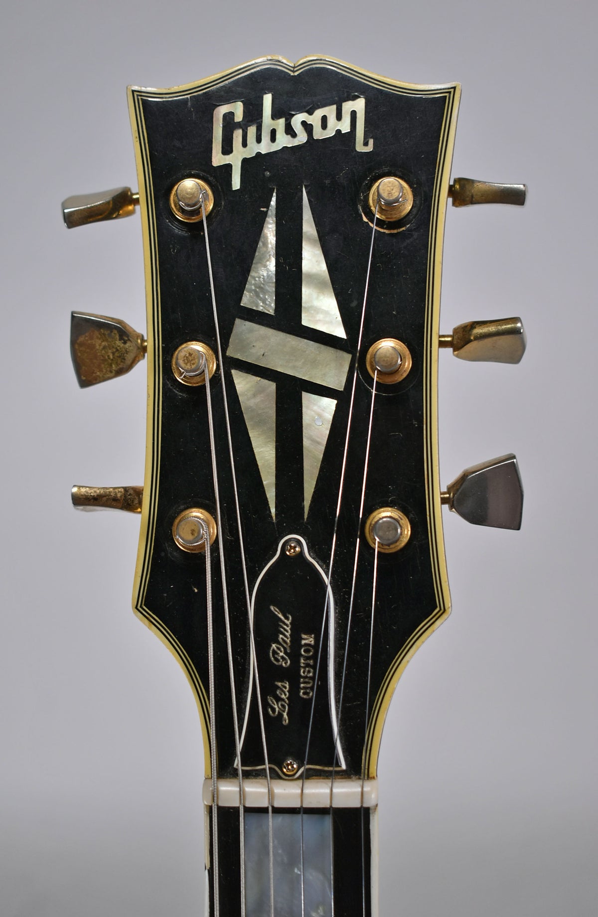 Close-up of the black headstock with mother-of-pearl inlays, gold tuners with tarnished metal buttons, and light binding wear.