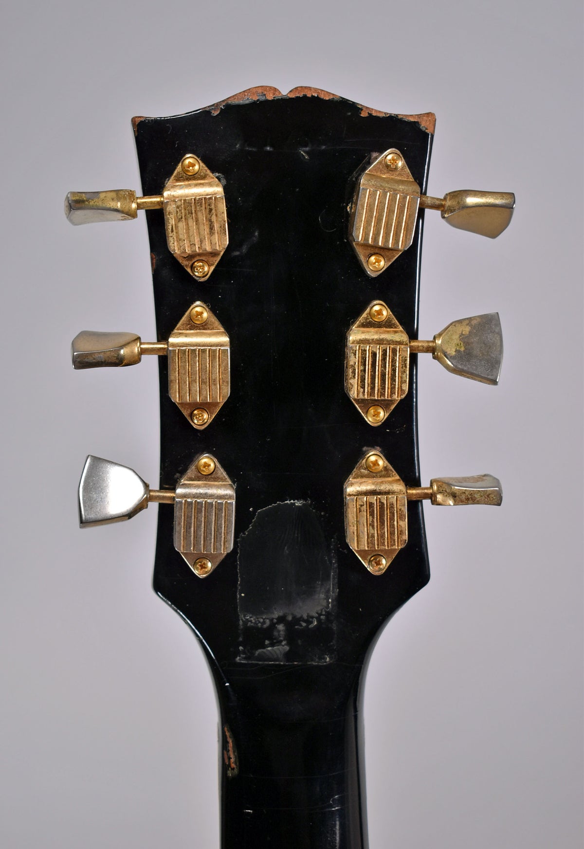 Rear view of the black headstock and neck, showing six gold-plated tuners with trapezoid housings and worn metal buttons.